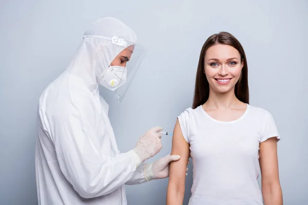 Foto pasien muda positif wanita ahli virologi menginjeksikan bahu penangkal covid eksperimental vaksin memakai penutup kepala seragam plastik perlindungan warna abu-abu terisolasi latar belakang — Stok Foto