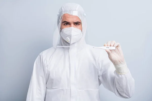 Photo of serious guy expert doc virology hold thermometer border airport control pasażerowie przyjazdy nosić maskę twarzy garnitur plastikowe oczy ochrony twarzy nos odizolowany szary kolor tła — Zdjęcie stockowe