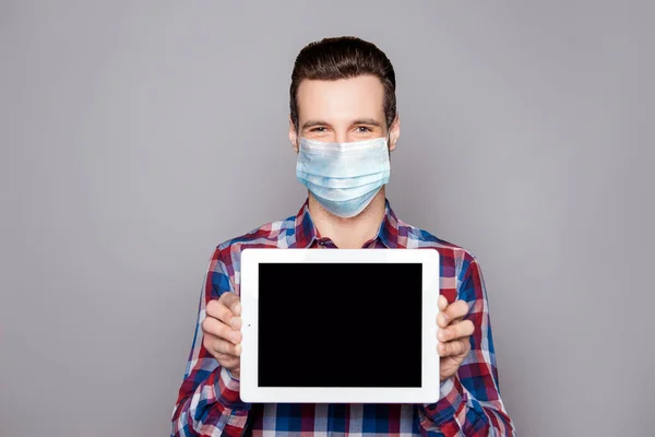 Close-up portrait of his he nice attractive glad cheerful guy wearing checked shirt protective mask showing tablet screen advert isolated over grey pastel color background — Stock Photo, Image