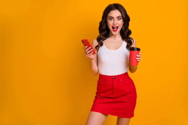 Foto de la señora bonita divertida sostener taza de café para ir mantener el teléfono leer nuevo post blogger sitio web desgaste casual blanco camiseta roja falda aislada de color amarillo brillante fondo — Foto de Stock