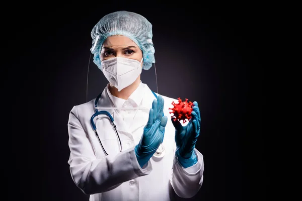 Photo of beautiful lady doc raise palm hold covid bacteria mutation not accept deny any experiments wear gloves mask coat facial plastic surgical cap isolated black color background