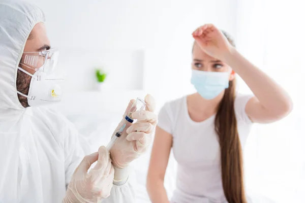 Closeup photo of young sick patient lady unwell touch forehead emergency doc virologist prepare antibiotic injection vaccine medication wear latex gloves protective uniform bedroom indoors — Stock Photo, Image