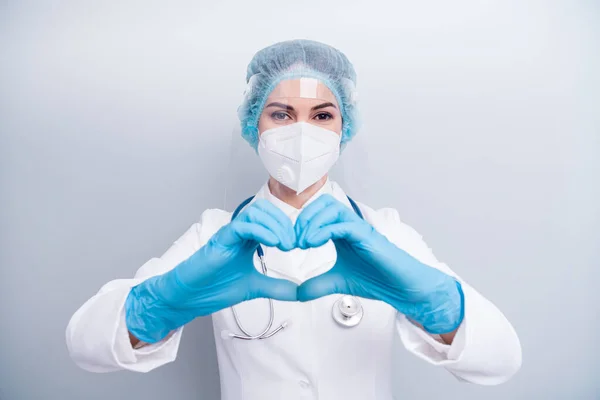 Photo of beautiful lady doc hospital making arms fingers heart figure good mood cardiac safety concept wear gloves mask coat facial plastic shield surgical cap isolated grey color background — Zdjęcie stockowe