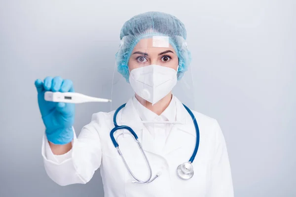 Φωτογραφία της νόσου της λοίμωξης ιολόγος γιατρός κυρία κρατήστε το θερμόμετρο μεγάλα μάτια υψηλής θερμοκρασίας φθορά παλτό μάσκα αναπνευστήρα προσώπου πλαστική προστασία χειρουργικά γάντια καπέλο απομονωμένο γκρι φόντο — Φωτογραφία Αρχείου