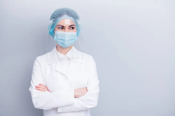 Foto de atractiva confianza virólogo doctor señora brazos cruzados buen humor mirada lado espacio vacío desgaste médico laboratorio abrigo máscara facial plástico protección tapa quirúrgica aislado gris fondo — Foto de Stock