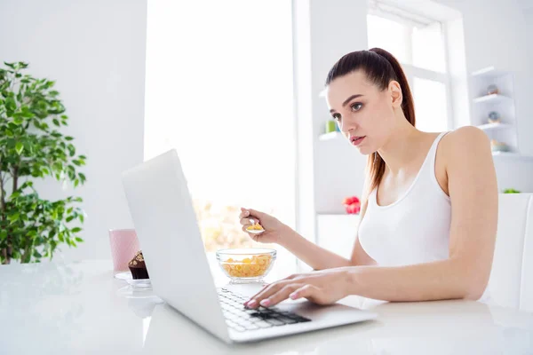 Profil fotografie okouzlující dům žena žena pracovník sedí ráno kuchyně prohlížení notebook freelancer mají snídani jíst cereálie kukuřice vločky zůstat doma vzdálenost vzdálená práce karanténa uvnitř — Stock fotografie