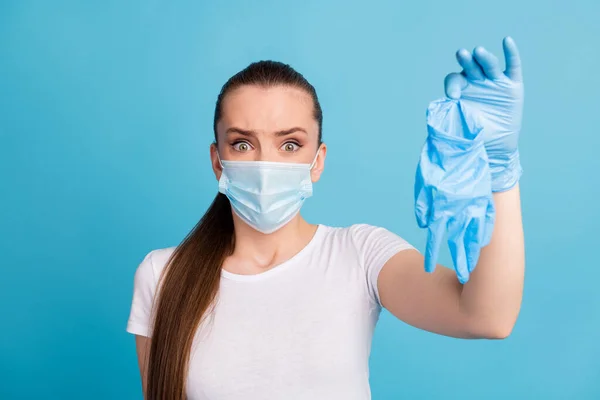 Close-up foto van mooie geschokte dame houden vuile chirurgische latex handschoenen bang covid infecties walgelijke uitdrukking dragen beschermen gezicht masker wit t-shirt geïsoleerde blauwe kleur achtergrond — Stockfoto