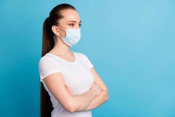 Foto van zelfverzekerde beweren dame armen gekruist kijken kant lege ruimte geïnteresseerd serieuze expressie dragen beschermen gezicht medisch masker wit t-shirt geïsoleerde blauwe kleur achtergrond — Stockfoto