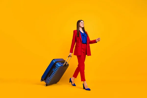 Full size profiel foto van aantrekkelijke zakelijke dame lopen luchthaven vlucht registratie rollende koffer slijtage specs rode luxe blazer blouse broek pak schoenen geïsoleerde gele kleur achtergrond — Stockfoto