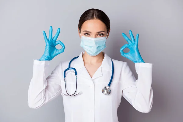 Zdjęcie atrakcyjnego lekarza wirusologa doświadczonego profesjonalistę pokazującego symbole okey ręce odpowiadają na wyniki badań pacjentów noszą mundur medyczny stetoskop laboratoryjny odizolowane szare tło — Zdjęcie stockowe