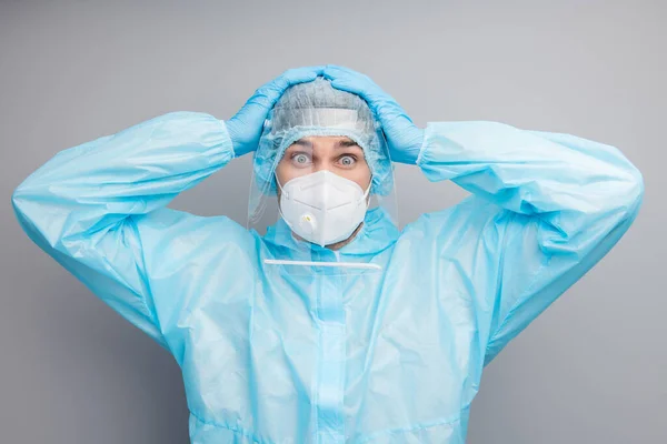 Foto de un chico experto doc centro de virología ojos grandes llenos de miedo sostenga los brazos en la cabeza use máscara respiratoria hazmat azul uniforme traje plástico facial protector escudo aislado color gris fondo — Foto de Stock