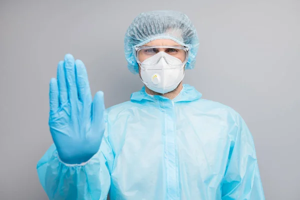 Foto de hombre experto doc virólogo celebrar pacientes parada de la palma entrar en peligro infectados zona usar guantes máscara hazmat azul uniforme quirúrgica gorra gafas aislado gris color fondo — Foto de Stock