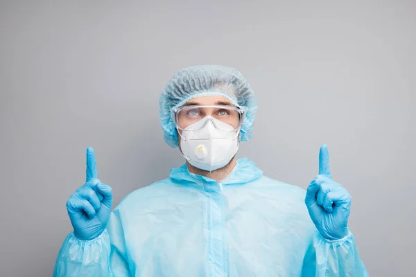 Close up photo of guy doc virolog direct fingers look up empty space przypominają czas szczepienia pacjenci noszą maskę hazmat blue uniform suit ochronne gogle odizolowane szary kolor tła — Zdjęcie stockowe