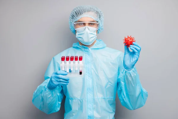 Foto de hombre experto doc virólogo celebrar pacientes sonda de sangre tubos covid bacteria gripe desgaste máscara hazmat azul uniforme quirúrgica gorra gafas aislado gris color fondo — Foto de Stock