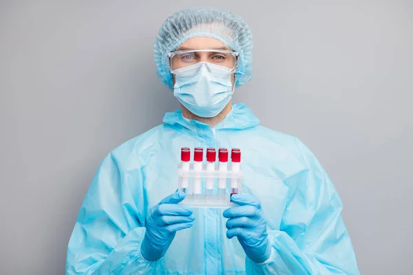 Foto de hombre experto doc virólogo mantenga enfermos pacientes covid sonda de sangre tubos examinando los resultados desgaste máscara hazmat azul uniforme traje de la tapa quirúrgica gafas aisladas de color gris fondo — Foto de Stock