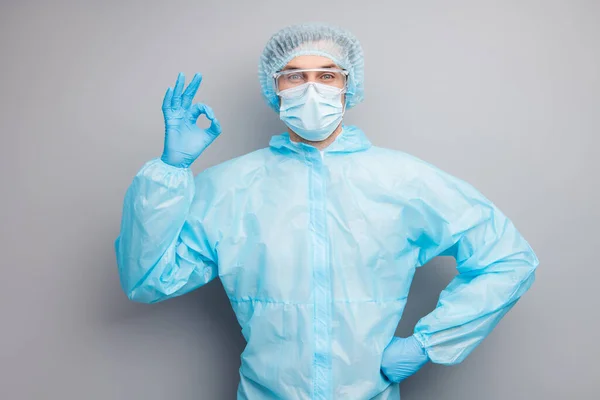 Фотографія впевненого хлопця-експерта вірусолога лікарського центру клініки професіонала, що показує символ джакузі пацієнта вдягають маску з рівномірним костюмом пластикові окуляри для обличчя ізольовані сіро-кольоровий фон — стокове фото