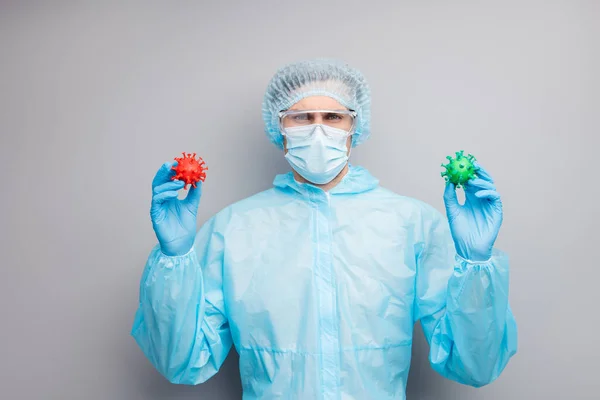 Photo of serious guy expert doc virology center hold two different bacteria hands vaccine research wear mask hazmat uniform surgical cap suit facial goggles isolated grey color background — Zdjęcie stockowe