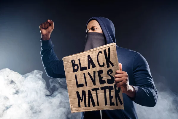 Profile side photo of crazy afro american rebellion man hold banner raise fists encourage fight human rights african community isolated black fog color background — Stock Photo, Image