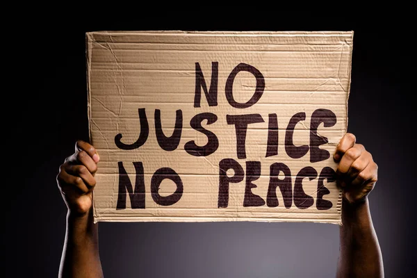 Photo rapprochée d'une personne afro-américaine tenant une bannière en carton avec du texte aucune justice aucune paix continuer à lutter message isolé sur fond de couleur noire — Photo