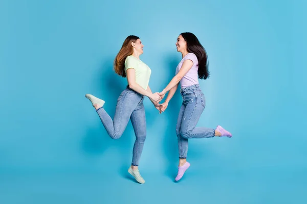 Full body profil zdjęcie dwóch osób lesbijki para panie skakać wysoki trzymać ramiona patrzeć oczy dobry nastrój szczęśliwy razem nosić casual t-shirty dżinsy obuwie odizolowany niebieski kolor tło — Zdjęcie stockowe