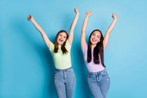 Foto von fröhlich attraktiv lustig verrückt zwei Menschen Damen Lesben Geschlecht Paar hebt die Fäuste nach oben überglücklich Bildungserfolg tragen lässig T-Shirts Jeans isoliert blaue Farbe Hintergrund — Stockfoto