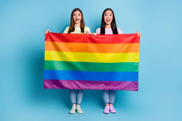 Teljes méretű fotó vicces vidám leszbikusok pár jött külföldi felvonulás támogatás tolerancia azonos nemű házasságok tartani meleg szivárvány zászló viselni alkalmi pólók farmer elszigetelt kék háttér — Stock Fotó