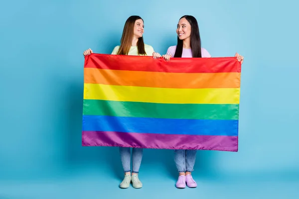 Teljes test fotó vicces trükkös leszbikusok pár látogasson el külföldi felvonulás támogatás azonos nemű házasságok tartani meleg szivárvány zászló megjelenés szem viselnek alkalmi pólók farmer elszigetelt kék háttér — Stock Fotó