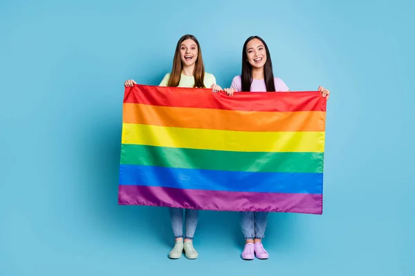 Teljes hosszúságú fotó vicces ingyenes szerelem leszbikusok pár jött külföldi felvonulás támogatás tolerancia azonos nemű házasságok tartani meleg szivárvány zászló viselése alkalmi pólók farmer elszigetelt kék szín háttér — Stock Fotó