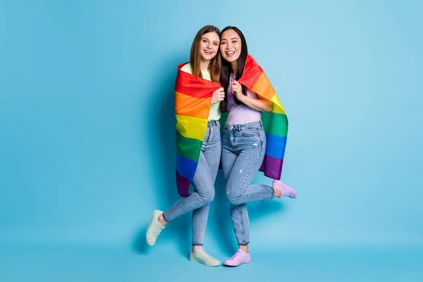 Πλήρης φωτογραφία μέγεθος της χαριτωμένης ελευθερίας λεσβίες ζευγάρι κυρίες ήρθε στο εξωτερικό παρέλαση δείχνουν ανοχή του ιδίου φύλου γάμους αγκαλιά γκέι σημαία ουράνιο τόξο φορούν casual t-shirts τζιν απομονωμένο μπλε χρώμα φόντο — Φωτογραφία Αρχείου
