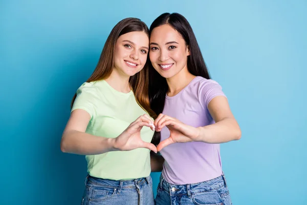 Photo of affectionate lesbians couple young ladies spend romance date make arms fingers heart shape lovers celebrate anniversary wear casual t-shirts jeans isolated blue color background — Stock Photo, Image