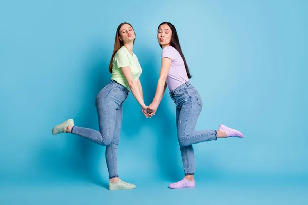 Full storlek profil foto av två tillgivna lesbiska par unga studenter gemenskap hålla armar skicka luft kyssar flirtig bära casual t-shirts jeans skor isolerad blå färg bakgrund — Stockfoto