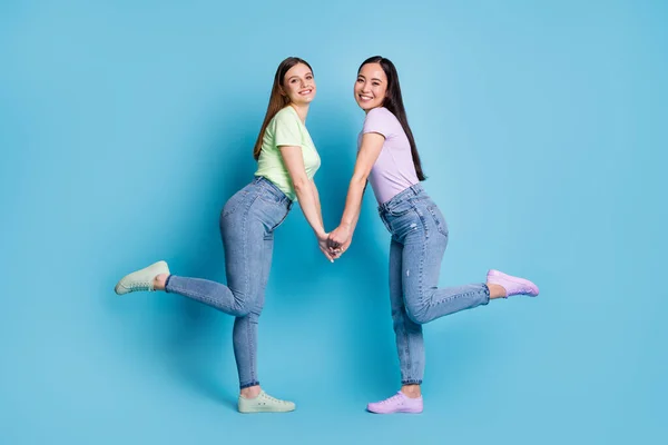 Full body profiel foto van twee aanhankelijke lesbiennes paar jonge studenten fellowship vrienden houden armen dragen casual t-shirts jeans schoeisel geïsoleerde blauwe kleur achtergrond — Stockfoto