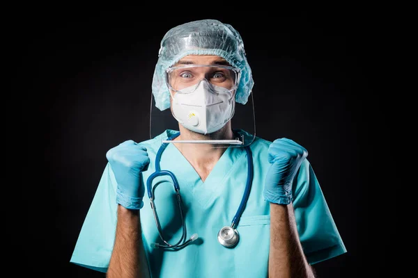 Photo of guy doc surgeon successful professional happy emotions raise fists wear mask uniform suit gown plastic facial goggles surgical cap isolated black color background