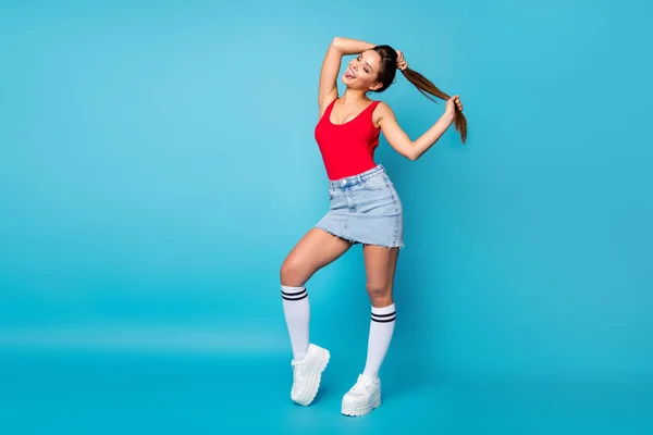 Full size foto positief meisje student voor te bereiden vrije tijd lopen maken staarten kapsel genieten van nieuwe haren glad haar effect tong-out slijtage casual rode tank-top denim benen geïsoleerde blauwe kleur achtergrond — Stockfoto