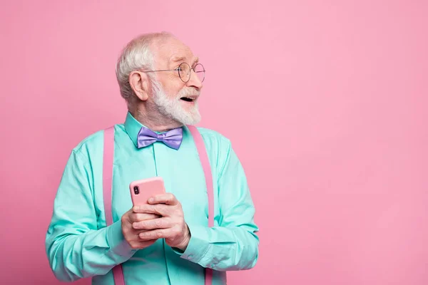 Vraiment, je comprends. Pensionné excité demander à la petite-fille en utilisant les réseaux sociaux tenir smartphone regard impressionné copyspace porter tenue turquoise noeud papillon violet isolé couleur rose pastel fond — Photo