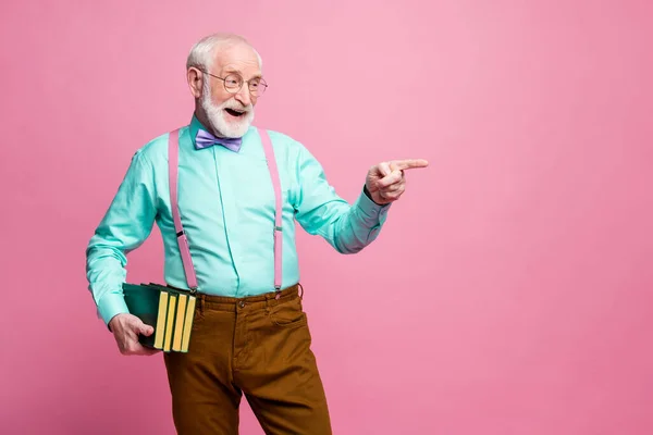 图片：有趣的爷爷教授的书大学教授的书大学直接手指空白处选择学生作答穿斑点衬衫吊袜带领结裤孤立的粉色彩色背景 — 图库照片
