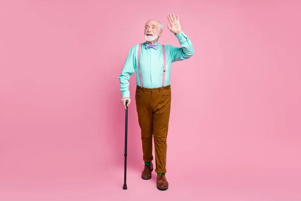 Full size foto van koele opa bewegen straat met behulp van wandelstok zwaaien arm zie vrienden dragen shirt bretels strik broek schoenen sokken geïsoleerde roze pastel achtergrond — Stockfoto