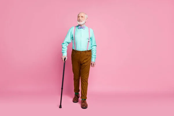 Foto de cuerpo completo de fresco abuelo buen humor caminar calle con la ayuda de bastón de caminar llevar camiseta de menta tirantes pajarita corbata pantalones marrones zapatos calcetines verdes aislados rosa pastel fondo — Foto de Stock