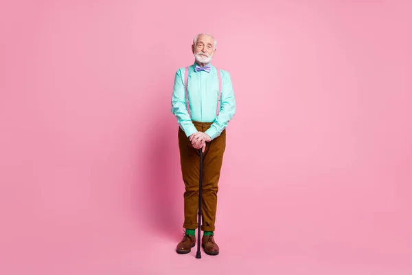 Pleine photo du corps de cool papy bonne humeur stand confiant avec bâton de marche usure menthe chemise bretelles noeud papillon brun pantalon chaussures chaussettes vertes isolé rose fond pastel — Photo