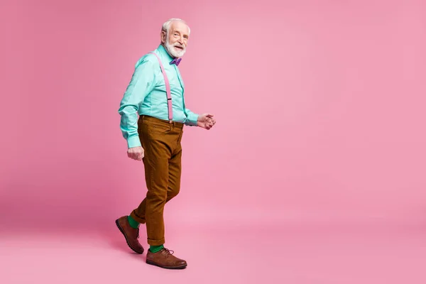 Foto de perfil de comprimento total de elegante vovô bom humor andando rua desgaste hortelã camisa suspensórios arco gravata marrom calças calçados verde meias isolado cor rosa fundo — Fotografia de Stock