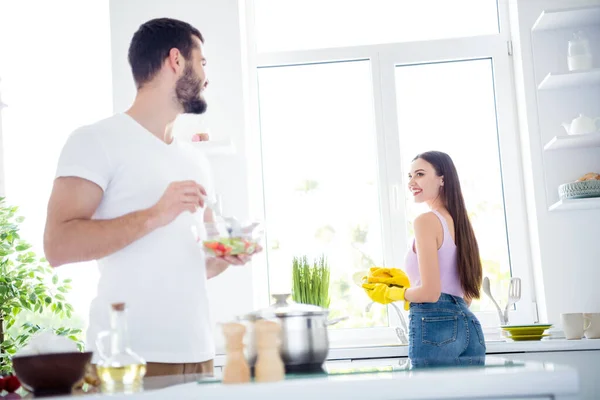 Hátsó gerinc nézet fotó két ember idilli házastársak férfi mix fűszerezés egészséges táplálkozás tál saláta ebéd nő mossa piszkos tányérok sárga gumi latex kesztyű marad otthon konyha házban — Stock Fotó