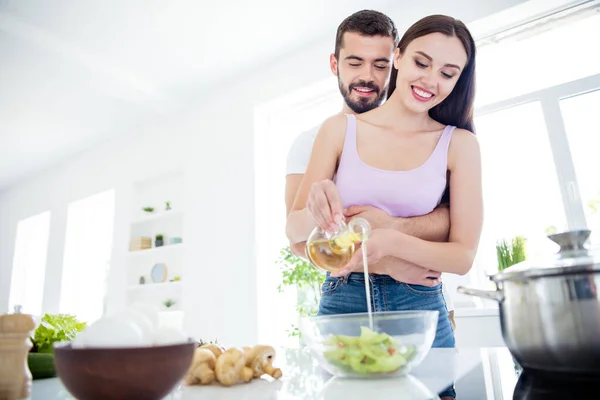Låg vinkel visa foto av två personer makar stanna hemma karantän förbereda maträtt lunch färsk sallad man kram omfamna kvinna hälla olja skål i huset kök inomhus — Stockfoto