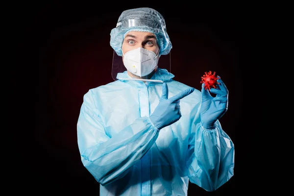 Zdjecie overjoyed facet doc wirusolog bezpośredni palec pokazujący covid bakterie szczepionka antidotum niwecznik nosić maskę hazmat niebieski mundur chirurgiczny czapka twarz tarcza odizolowany czarny kolor tło — Zdjęcie stockowe