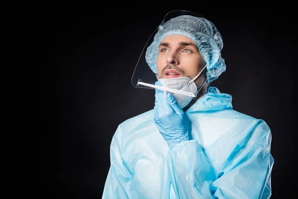 Zdjęcie zmęczonego doktorka wirusolog facet wyczerpany leczyć chorych pacjentów covid przytłoczony zdjąć maskę nosić hazmat niebieski mundur garnitur plastik twarz tarcza odizolowany czarny kolor tło — Zdjęcie stockowe