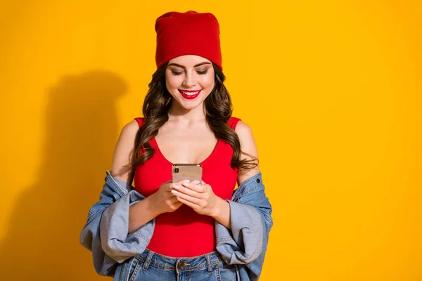 Retrato de tendência alegre positiva jovem millennial girl usar tipo de smartphone ler compartilhar notícias da rede social desgaste vermelho headwear singlet isolado sobre fundo de cor brilhante — Fotografia de Stock