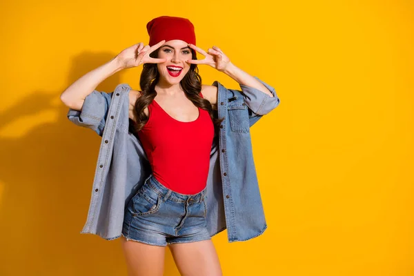 Portret van positief vrolijk openhartig jong meisje genieten weekend vrije tijd maken v-teken dragen goed kijken rood hoofddeksel denim singlet geïsoleerd over heldere kleur achtergrond — Stockfoto