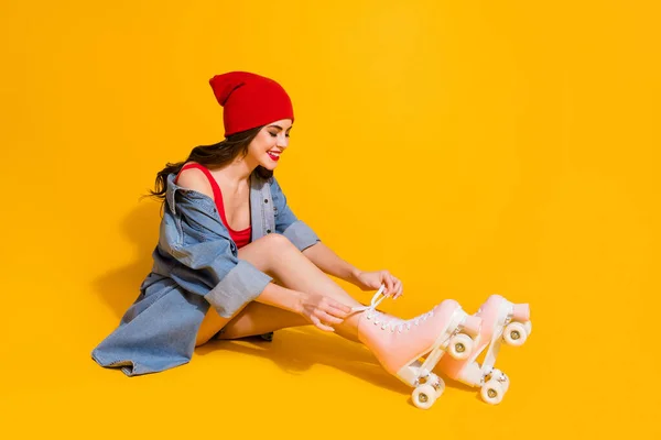 Full size profiel zijkant foto van positieve jeugd millennial meisje zitten vloer stropdas veters rolschaatsen dragen rode hoofddeksel singlet jeans shorts geïsoleerd over heldere kleur achtergrond — Stockfoto