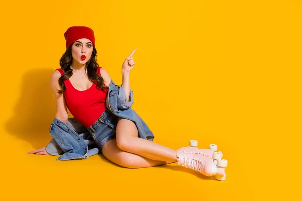 Full length foto di sorpreso studente ragazza sedersi pavimento indicare annunci promozionali impressionato urlo wow omg usura rosso copricapo serbatoio-top pattini a rotelle denim isolato colore brillante sfondo — Foto Stock