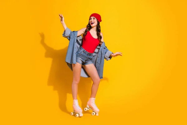 Full size foto van vrolijke funky tiener jeugd student meisje genieten van de lente vrije tijd weekend roller geschaatst rijden dragen rode hoofddeksel jeans singlet geïsoleerd over heldere kleur achtergrond — Stockfoto