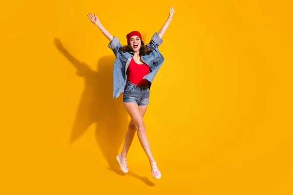 Neşeli, enerjik genç kız zıpla. Kırmızı başlık giy. Parlak renkli arka planda izole edilmiş kot ayakkabılar giy. — Stok fotoğraf